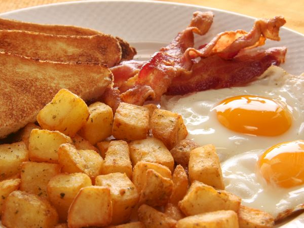 A hearty breakfast plate: hash browns or crispy potatoes, sunny-side eggs, buttered toast, and crispy bacon on the side.