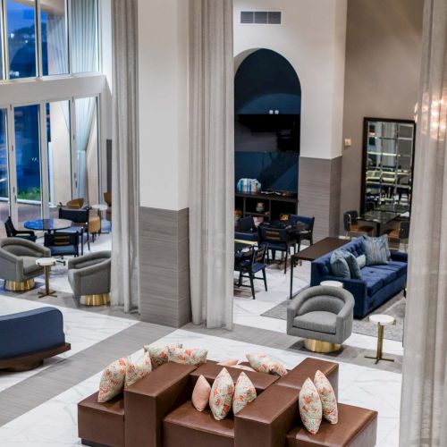 A stylish hotel lobby with plush seating, a brown sofa set around a coffee table, tall arches, and a bright, modern lounge area.