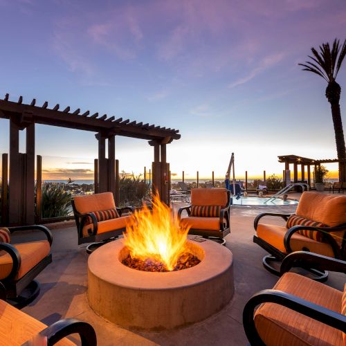 A cozy outdoor lounge with a fire pit, low seating, string lights, and a pebbled patio under a clear night sky, perfect for gatherings.