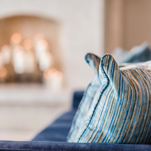 A striped throw pillow on a blue couch in a cozy living room with a glowing fireplace in the background.