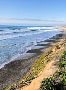 Bright sunlit coastal path with rocky shore, turquoise sea, and grassy cliffs. A scenic seaside walk along the edge of the cliffs.