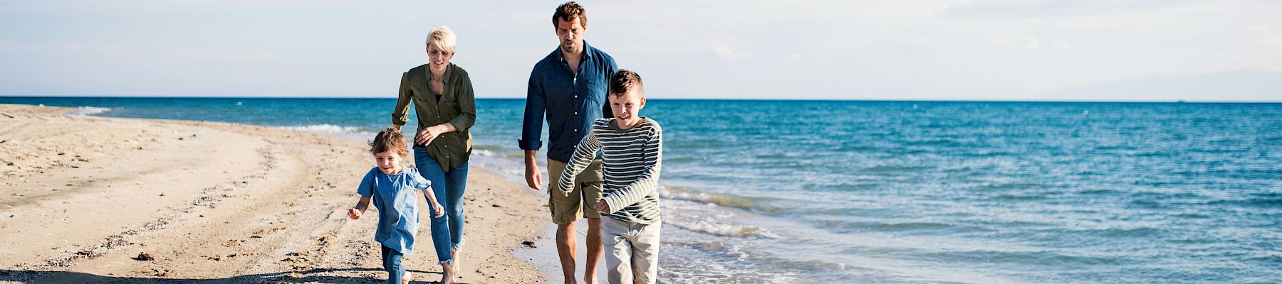 A family of four walks along a sunny beach, waves lapping at their feet, as they enjoy a seaside stroll together.